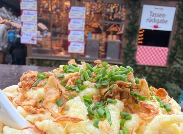 Cheesy German Kaesespaetzle topped with fried onions and chives at a festive Christmas market stall.
