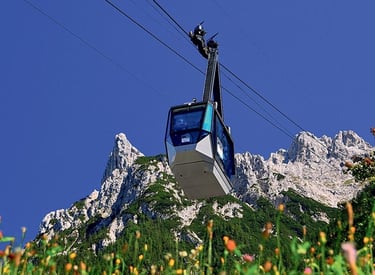 Cable car gondola ascending towards rugged mountain peaks in the Alps under a clear blue sky.