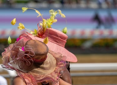 Elegant women wearing decorative Kentucky Derby style hats at a horse racing track.