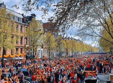 Crowds in orange clothing celebrate King's Day along the historic Amsterdam canals and city streets.