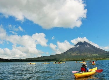 Tourists in yellow kayaks paddle on Lake Arenal with the Arenal Volcano in the background.