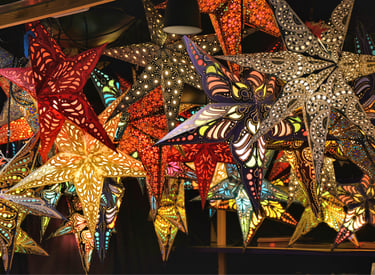 A vibrant display of illuminated paper star lanterns with intricate cutouts hanging at a Christmas market.