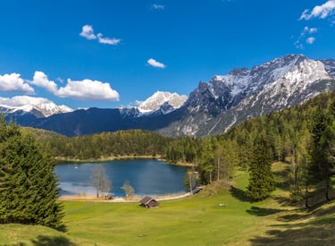 Scenic view of Lautersee lake in the Bavarian Alps with snow-capped mountains and evergreen pine forests.