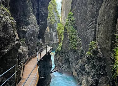 A narrow wooden walkway along steep rock walls above a turquoise river in a mountain gorge.