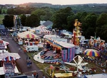 Aerial view of a colorful outdoor carnival with amusement park rides, game booths, and striped tents.