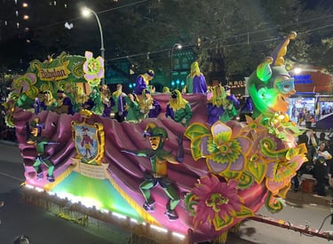 A colorful Mardi Gras float with masked riders and jester decorations in a New Orleans parade.