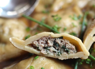 A sliced German Maultasche dumpling filled with minced meat and spinach, garnished with fresh chives.