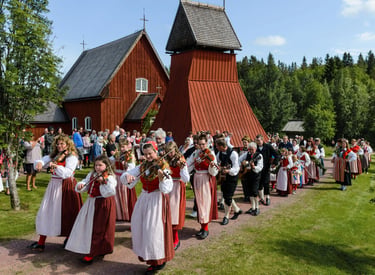 Traditional Swedish musicians in folk costumes playing violins outside a historic red wooden church.