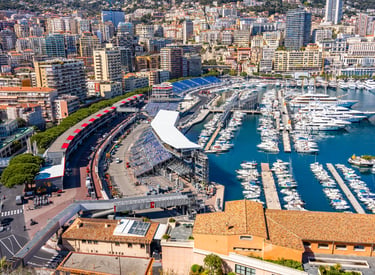Aerial view of Port Hercules in Monaco featuring luxury yachts, the Formula 1 Grand Prix circuit, and city skyline.