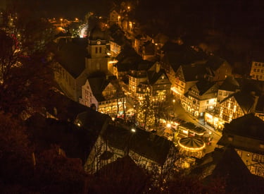 Aerial night view of a German Christmas market with half-timbered houses and festive lights.
