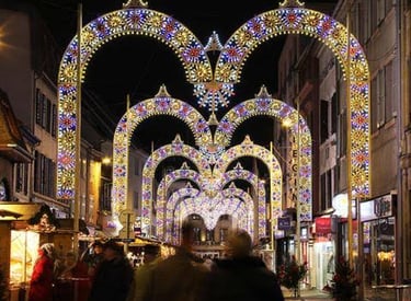 Illuminated Christmas market street with festive light arches and holiday shoppers at night.