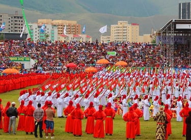 Performers in traditional Mongolian attire carry flags during a Naadam festival ceremony in a crowded stadium.