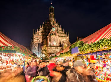 Nuremberg Christmas Market at night with crowds and the illuminated Frauenkirche cathedral.