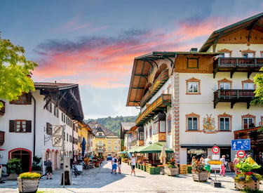 Charming Bavarian village street in Germany with traditional alpine architecture under a sunset sky.