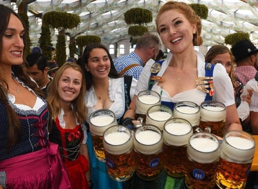 Smiling waitress in a traditional dirndl carrying several large mugs of beer at Oktoberfest.