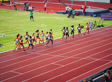 Professional female athletes competing in a long distance race on a red outdoor running track.