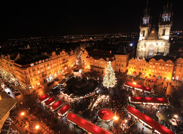 Aerial night view of Prague Old Town Square Christmas market with a glowing tree and Tyn Church.