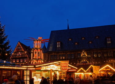 Crowded German Christmas market at night with festive lights, food stalls, and a traditional pyramid.