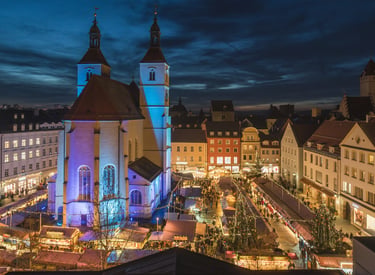Elevated view of a traditional German Christmas market at night with festive lights and a historic church.