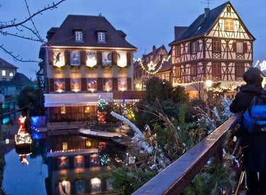 Scenic Colmar canal at dusk with festive Christmas lights and historic half-timbered houses.