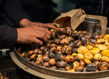 A street vendor's hands sorting hot roasted chestnuts in a large pan at a winter market.