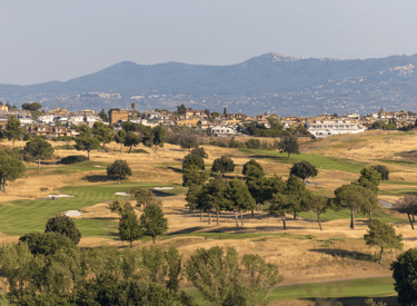 Scenic view of a lush golf course in Italy with rolling fairways, trees, and mountains in the background.