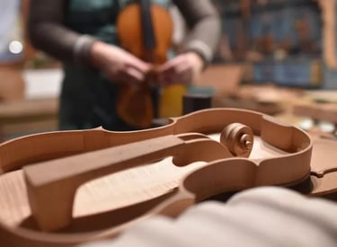 Handcrafted wooden violin body in a luthier workshop with a violin maker working in the background.