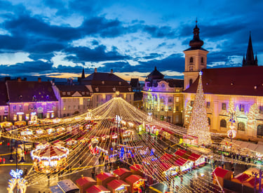 Sibiu Christmas Market at night featuring festive lights, a tall tree, and a carousel in the main square.