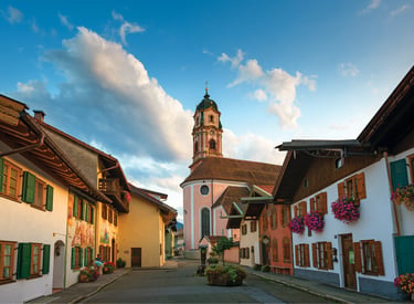 Traditional Bavarian houses with flower boxes lead to the historic St. Peter and Paul church in Mittenwald, Germany.