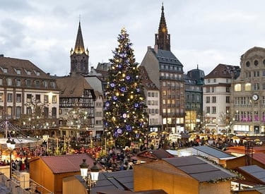 A giant lit Christmas tree stands in the center of the Strasbourg Christmas Market at dusk.