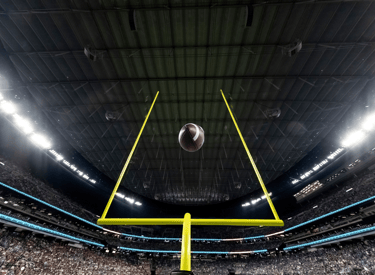 Low angle view of an American football flying through yellow goal posts in a crowded indoor stadium.