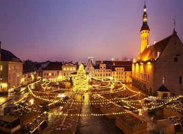 Tallinn Christmas market at dusk with glowing festive lights, a large tree, and historic town hall architecture.