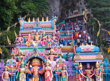 Colorful Hindu statues and tourists on the rainbow stairs at the Batu Caves temple in Malaysia.