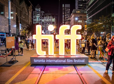 A glowing TIFF sign illuminates a crowded Toronto International Film Festival red carpet event at night.