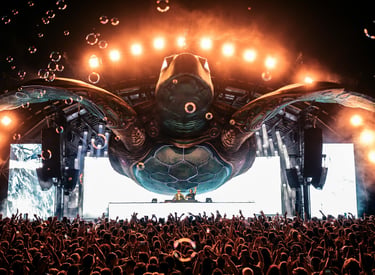 DJs perform on a massive sea turtle stage with bubbles and bright lights at a crowded music festival.