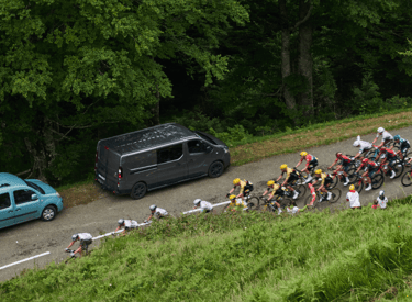 Professional cyclists racing in a peloton along a winding mountain road during a road cycling competition.
