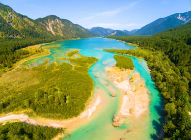 Aerial view of a turquoise alpine lake and river winding through lush green mountain valleys.