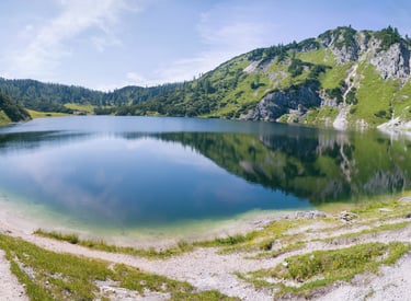 Panoramic view of a crystal clear alpine lake surrounded by green mountains and hiking trails.