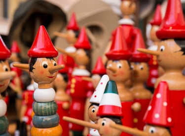 Handcrafted wooden Pinocchio dolls with red hats and long noses in an Italian souvenir shop.
