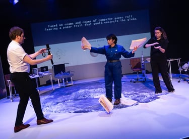 A white man, an Iranian woman in blue overalls and a BSL interpreter throw paper on the moon