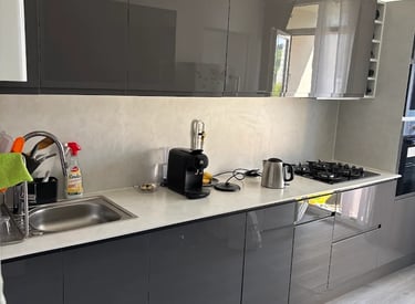 Cuisine moderne avec façades grises brillantes, plan de travail blanc, gazinière et machine à café.