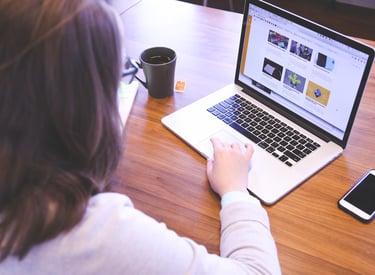 mulher-de-cabelos-lisos-sentada-de-costas-com-um-notebook-aberto-em-cima-de-uma-mesa
