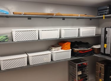 Prateleira contendo cestos organizadores, malas enfileiras, tudo bem organizado.
