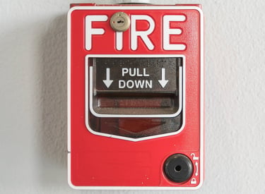 Estación manual roja de alarma contra incendios con texto blanco montada en una pared lisa.