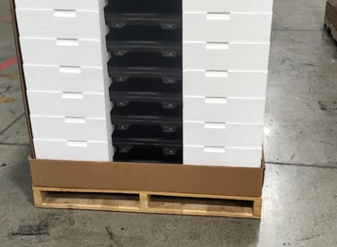 A stack of black glass panels securely packaged with white foam inserts on a wooden pallet.