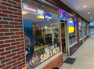 Exterior of Sava's Pizza storefront with neon beer signs and Pepsi logo on a brick building.