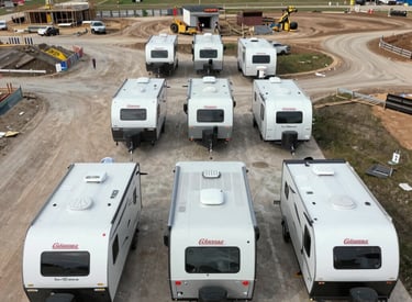 A sleek, modern Coleman-style camper in safety orange and dark teal parked at a rugged disaster response site.