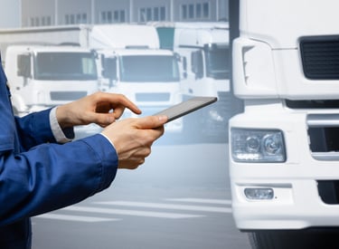 Logistics worker using tablet in front of white freight trucks — pilot delivery program coordination