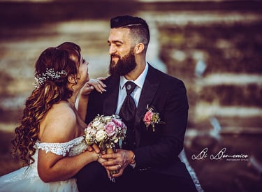 Mariés complices et souriants, robe bohème dentelle et costume noir, bouquet roses.