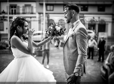 Mariée émue se couvre la bouche face au marié tenant le bouquet, N&B rue.